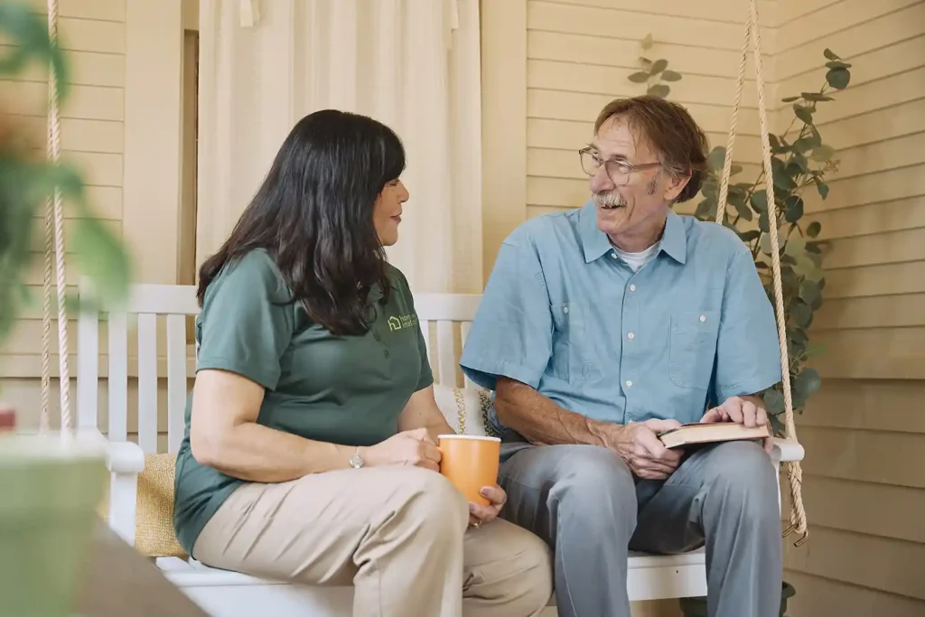 Home Instead caregiver and senior man having a warm conversation on porch swing