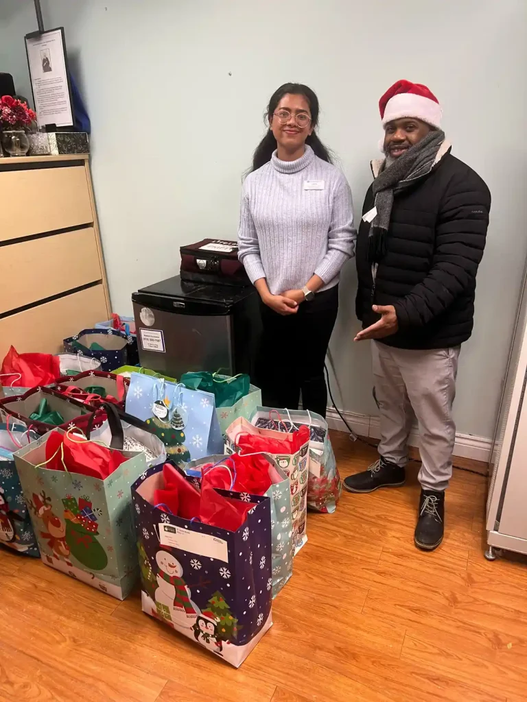 Home Instead Toronto East staff member and St. Clair O'Connor Community facility staff standing with festive gift bags prepared for senior residents